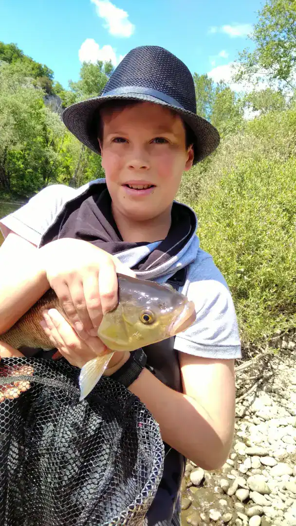 Jeune garçon tenant fièrement un poisson au bord de rivière